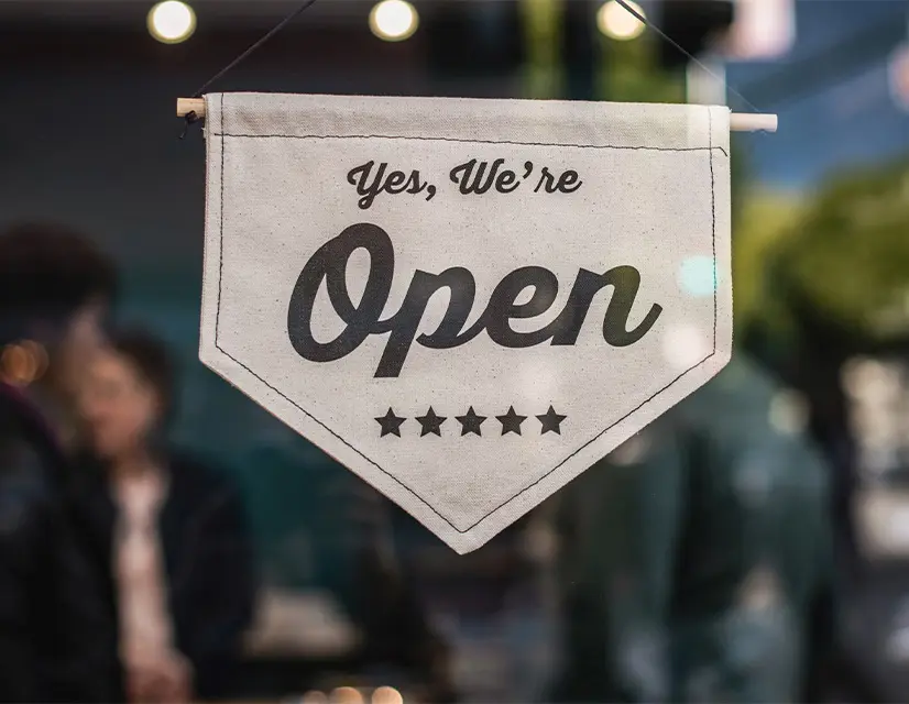 An image of a shop, with a sign on the door that reads Now Open.